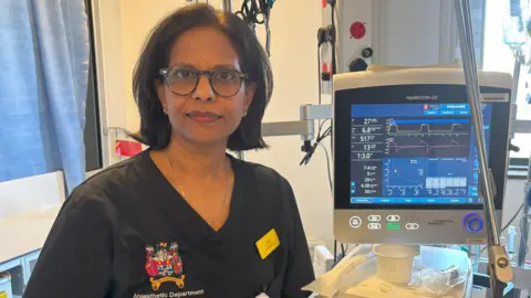 A female consultant standing in front of a computer monitor in scrubs