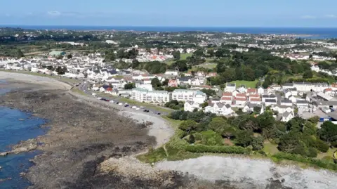 An aerial view of the Guernsey coastline. Showing houses and trees and beaches. 