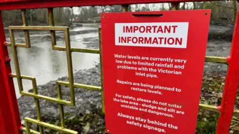 Red sign with white writing explaining the lake is closed for works to take place.