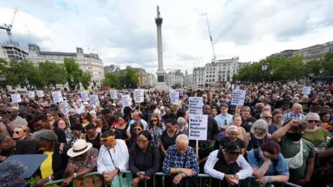 A crowd of people gather in Trafalgar Square as part of a vigil for Jason Arday. Some of them are holding placards.