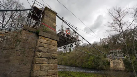 A complicated piece of scaffolding machinery has been set up between the two sides of a stone bridge to help rebuild it.