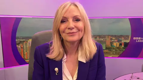 A woman with blond hair wearing a blue jacket and cream blouse