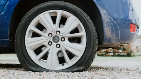 Getty Images A car wheel, with a tyre that may be flat in a pothole. The car is blue.
