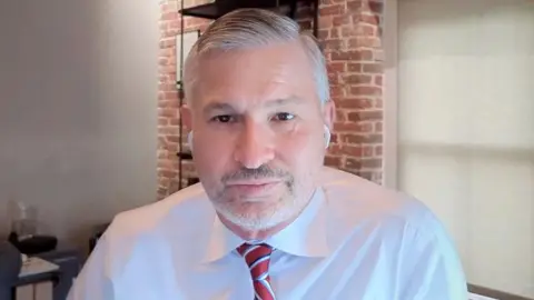 Makran's lawyer Tom Claire, a white man with gray hair, stubble and white shirt and red tie 