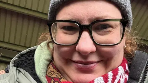 Keeley Wilson-Townsend A woman wearing glasses, a red scarf and a grey hat