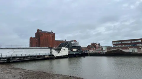Local Democracy Reporting Service A landscape shot of Corporation Bridge in Grimsby. It is a rolling lift bridge, which spans the River Freshney and connects Corporation Road and Victoria Street South. Buildings can be seen in the distance and the sky is overcast.