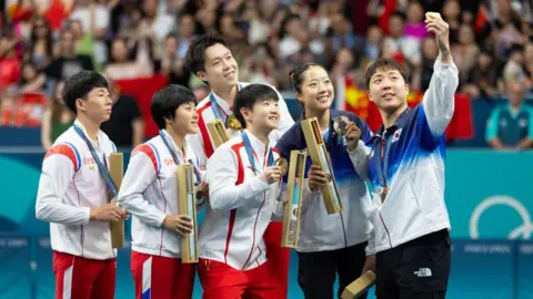 Getty Images A South Korean athlete takes a selfie with his teammate and duos from North Korea and China