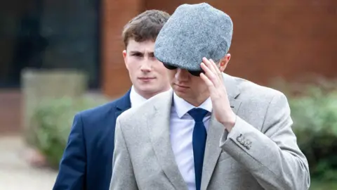 Phil Cannings - Newburytoday Two young men both seen wearing suits. One has a flatcap covering part of his face and is also wearing sunglasses. The other's face can be seen clearly.
Daniel Heath is seen on the right in a blue suit with his face uncovered - William Lawrence is seen on the left with a grey suit and blue tie.