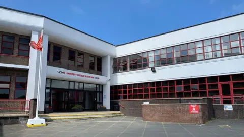 The outside of the front of main UCM building. It is on two floors and it white with lots of red-framed windows