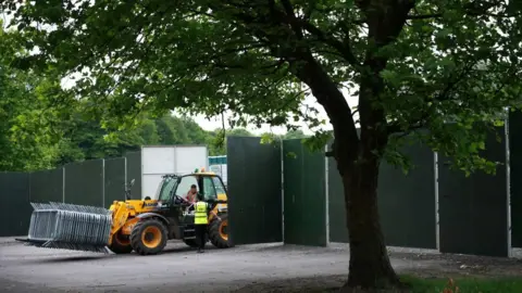 Reuters A person driving a forklift carrying metal barricades drives out between large barriers in a park.