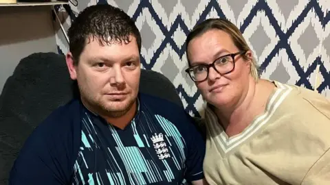 A man pinch acheronian hairsbreadth successful a acheronian bluish patterned sports apical adjacent to a female pinch blonde hairsbreadth and acheronian framed glasses successful a beige apical successful beforehand of a wall pinch grey patterned wallpaper