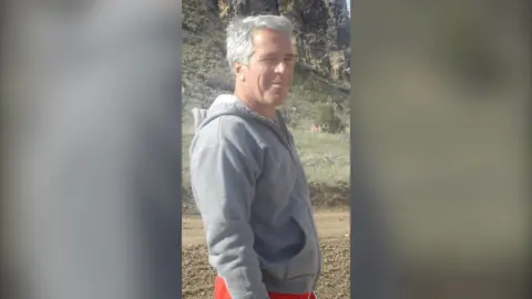 Jeffery Epstein has grey hair and is wearing a grey hoodie.