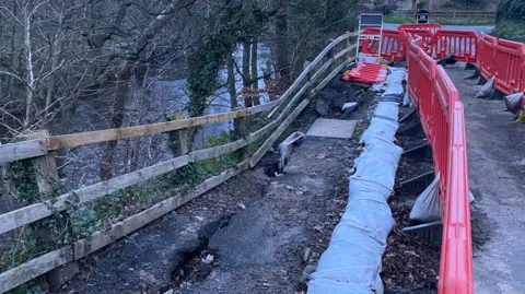 BBC A wooden fence partially collapsed into a river
