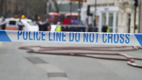 Getty Images Police Line Do Not Cross tape against blurred city background - stock photo