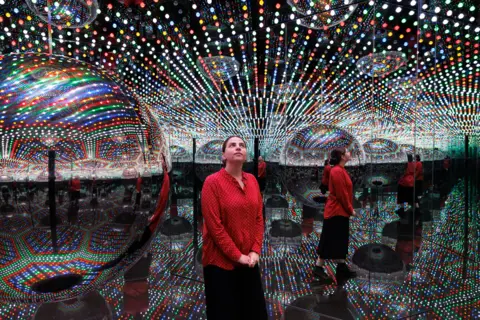Getty Images A visitor standing in one of Kusama's Infinity Rooms, seen reflected several times in mirrors surrounded by lights
