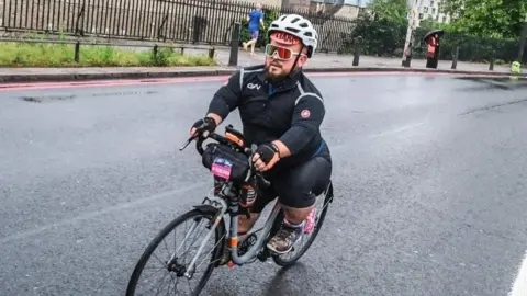 Sportograph A man with achondroplasia on a bike on the road with a helmet and reflective glasses on.