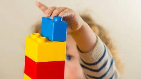 A young child plays with blue, yellow and red building blocks.
