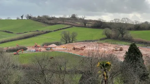A building site with plant machinery surrounded by fields