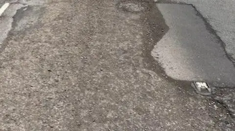 Derek Bennett Potholes: a rough patch in a grey road 