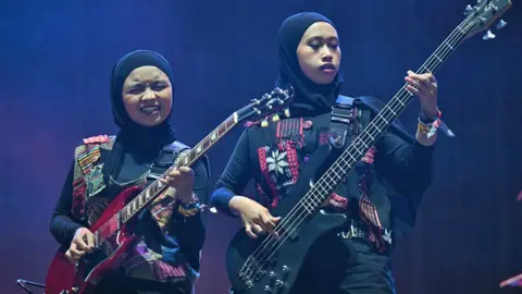 Getty Images Two members of Indonesian rock band Voice of Baceprot wearing hijabs play guitar on the Woodsies stage