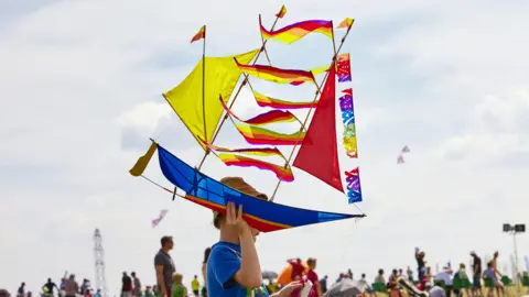 National Trust/Arnhel de Serra A child, wearing a hat, with a blue top on, holding a colourful kite, in the shape of a boat