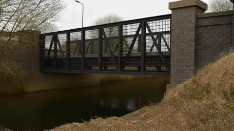 Rotherham Council A modern looking black metal footbridge above a narrow stretch of water
