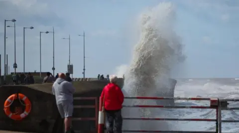 EPA People watch as waves crash over the sea wall in New Brighton