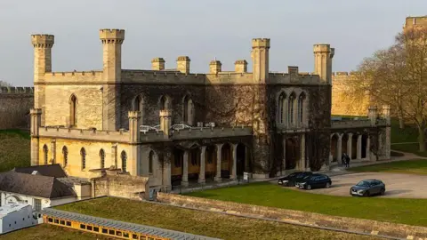 A view of the Lincoln Crown Court building taken from the medieval walls at Lincoln Castle. It is a stone building with castle‑like towers and arched windows, situated on a courtyard with a lawned area.
