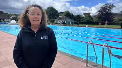 Julie Sergeant wearing a dark blue fleece stood to the left of the image with the pool and steps visible behind her. 