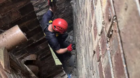 Cambs Fire and Rescue A firefighter is seen on a rope being lowered into a narrow gap between two brick buildings