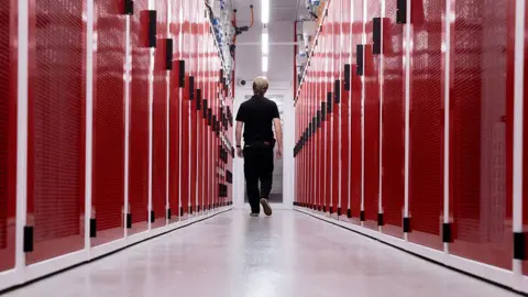 A worker at a data centre in Sydney, Australia, walking down the middle of two rows of red-faced computer servers