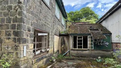 BBC/Lucy Ashton A derelict stone building with smashed windows is surrounded by scrubland and is vandalised