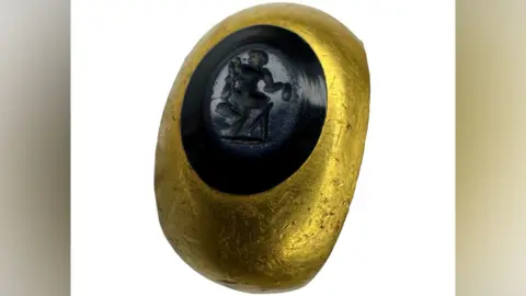 Hanson Ross The 2nd Century gold Roman intaglio ring set with an oval blue nicolo gemstone depicting a male figure seated right on a rock holding a purse in outstretched right hand. It has an estimated value of £1,000-£1,500, image courtesy of Hanson Ross