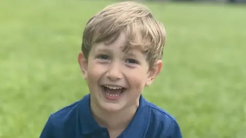 Family handout Benedict, a young boy with blond hair, is on a lawned space. He is wearing a blue polo shirt and is laughing into the camera.