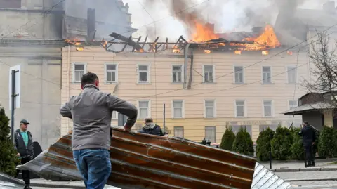 A man clears debris as a building burns in the background after Russian strikes on Lviv on Tuesday