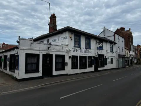 Martin Barber/BBC A white pub next to a road. It has several large windows on the front and the side. There are two doors. It is a cloudy day.