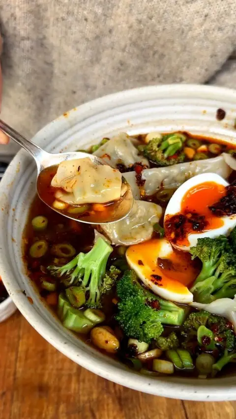 Bowl of soup containing green vegetables and eggs 