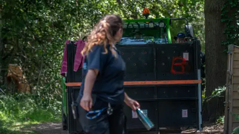 Bristol Zoo Project/PA A Bristol Zoo Project worker is walking in front of the forklift truck guiding it down a tree-lined road.