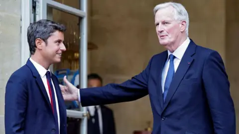 STEPHANE DE SAKUTIN/AFP O recém-nomeado primeiro-ministro Michel Barnier (R) cumprimenta o primeiro-ministro cessante Gabriel Attal (L) na cerimônia de transferência no Hotel Matignon em Paris, 5 de setembro de 2024.