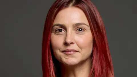 UK Parliament Melanie has long red hair and is semi-smiling into the camera