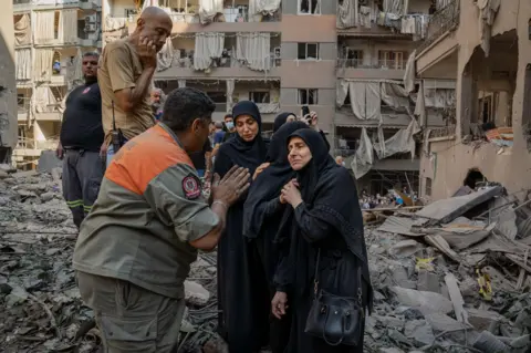 Joel Gunter/BBC Distraught residents speak to Youssef Al-Mallah, the head of the rescue team, at the site of the Basta strike.