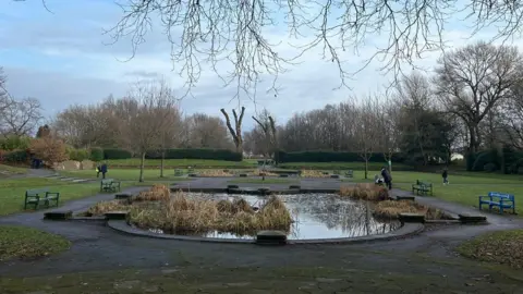 BBC / Kay Crewdson A large pond surrounding by a circular path, park benches and green fields. 