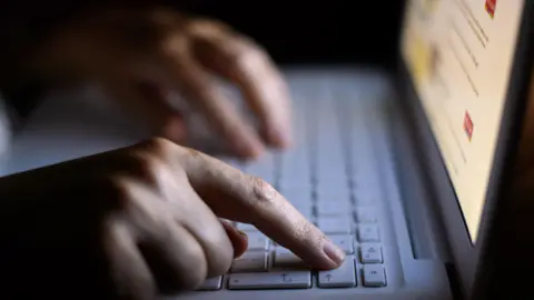 PA Media A person seen typing on a laptop in the dark with only the screen illuminating the scene.