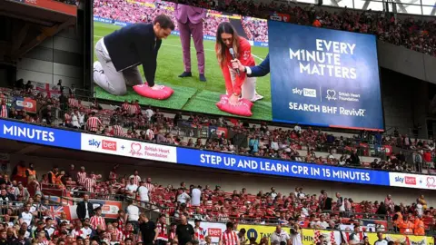 Getty Images Tom Lockyer performs a CPR technique demonstration on the LED screen at half-time during the Championship play-off final match between Sheffield United and Sunderland at Wembley Stadium.