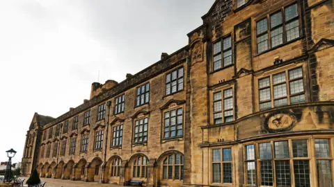 A historic brick building with three rows of windows and an ornate lamppost outside.