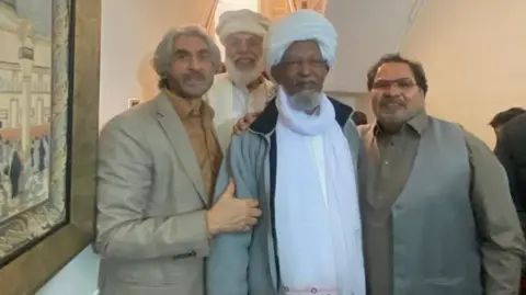 TOFAIL AWAN A group of four smartly dressed men gathered as part of Eid celebrations. They are wearing various forms of traditional Islamic dress.