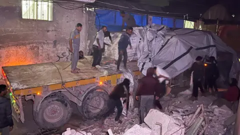 Palestinian workers unload sacks of flour from an aid lorry at a bakery in Khan Younis, southern Gaza (21 May 2025)