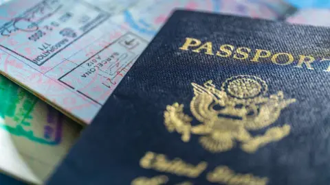 Close-up of the front of a US passport placed on top of an open passport page showing visa stamps.