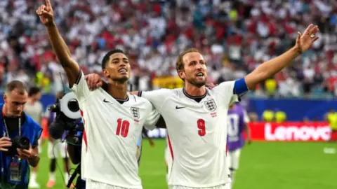 PA Media Jude Bellingham and Harry Kane, in their white England shirts, with their arms around each other as they salute the fans after being Norway
