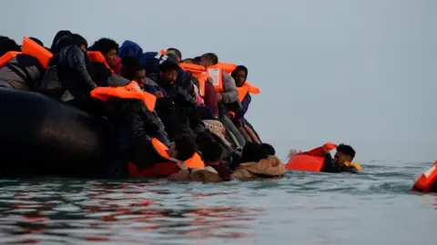 A group of people, all wearing life jackets, crowd onto an inflatable boat in the English Channel.